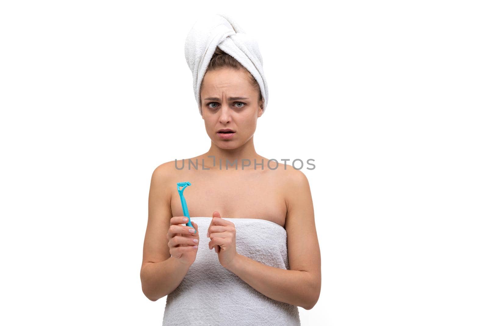 a young woman wrapped in a towel with a razor in her hands is afraid to shave.