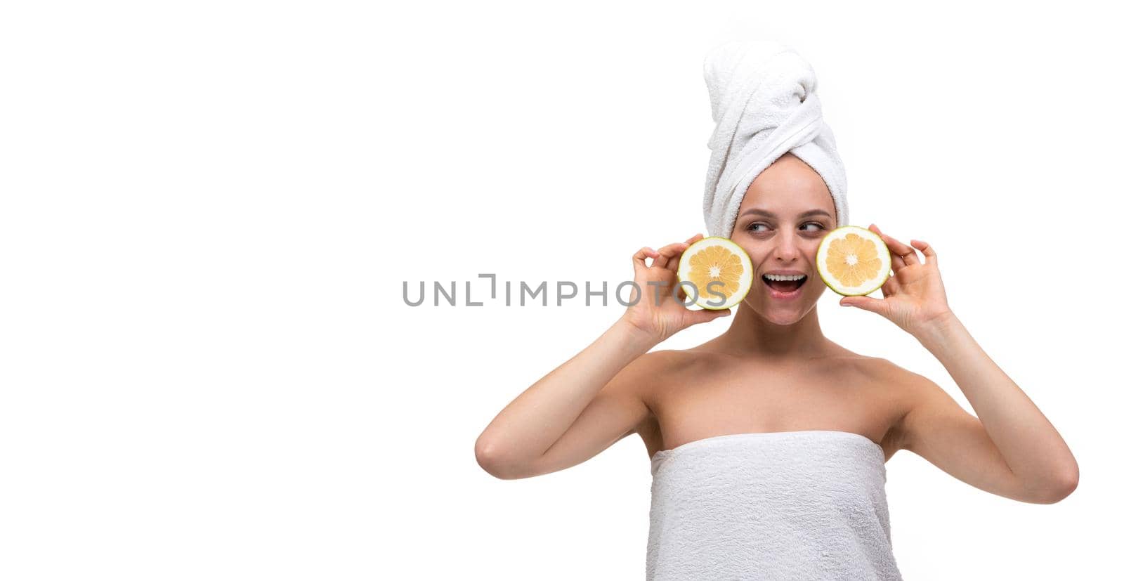 beautiful well-groomed young woman with a towel on her body after a shower with a smile looking at the camera holding oranges.