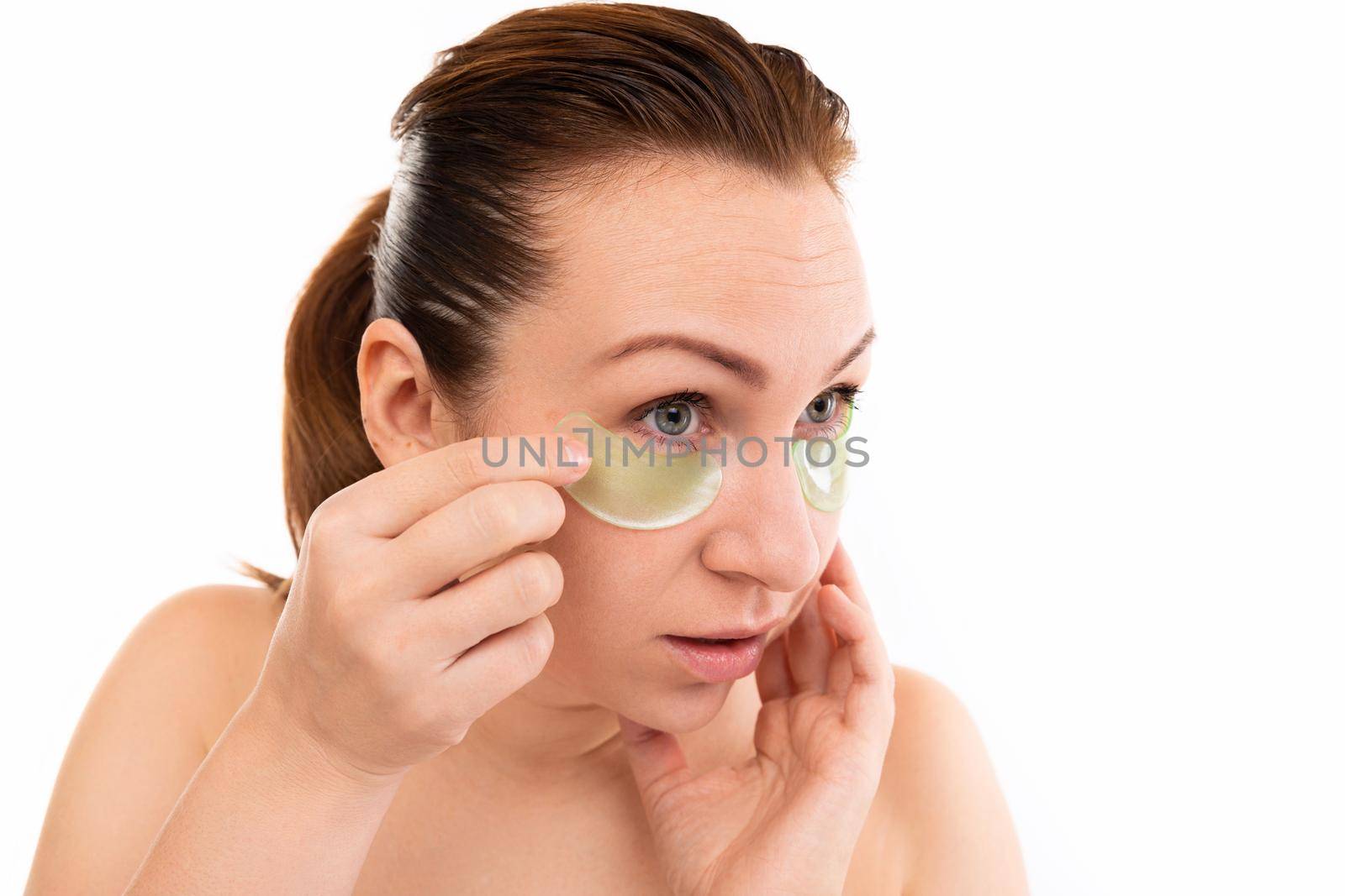 portrait of a woman on a white background after cosmetic procedures, removes cosmetic patches for skin care around the eyes.