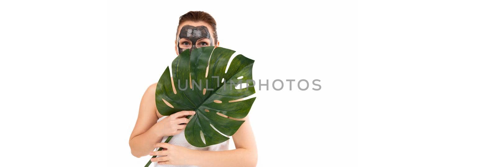 a woman with a black cosmetic mask on her face holds a green leaf in her hands.