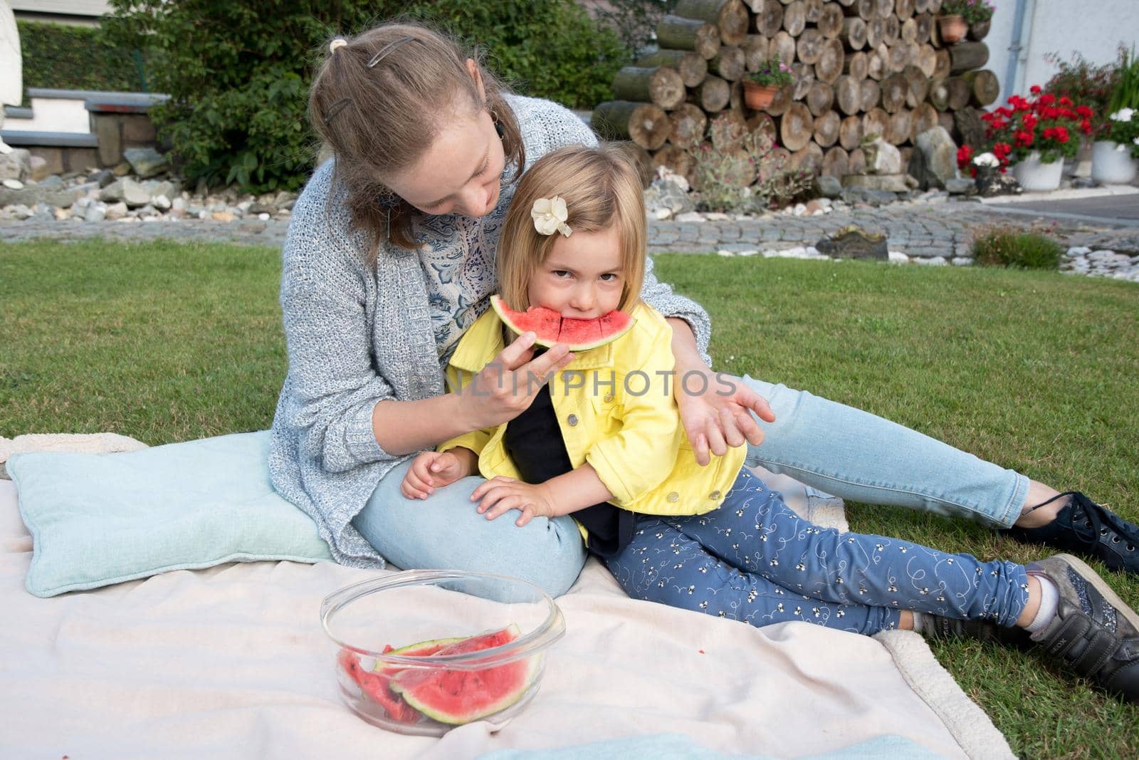 young mother feeds her daughter sweet watermelon, picnic in nature near the house by KaterinaDalemans