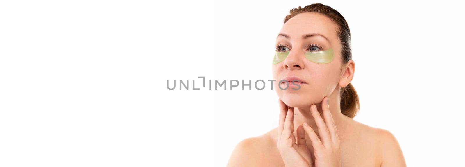 young woman on after cosmetic procedures touches the skin of the face with her hands, under the eyes cosmetic patches of light green color by TRMK
