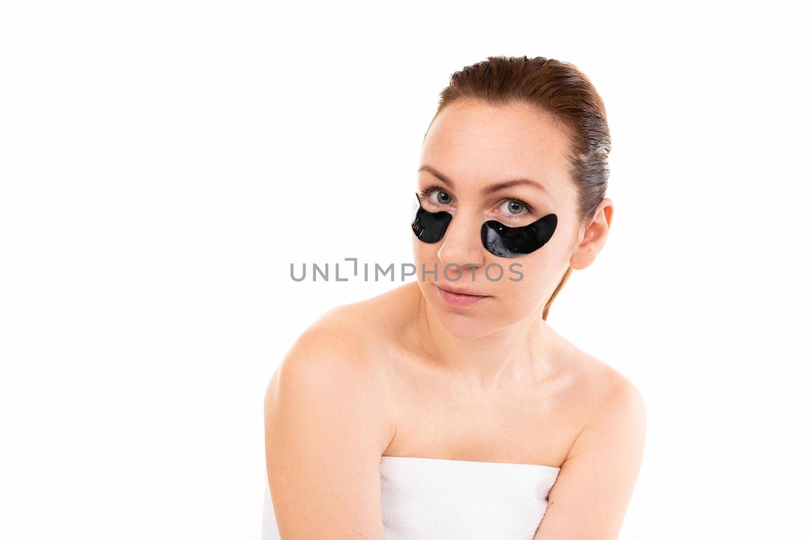 young woman in a towel after cosmetic procedures on the background of a white wall with looking at the camera.