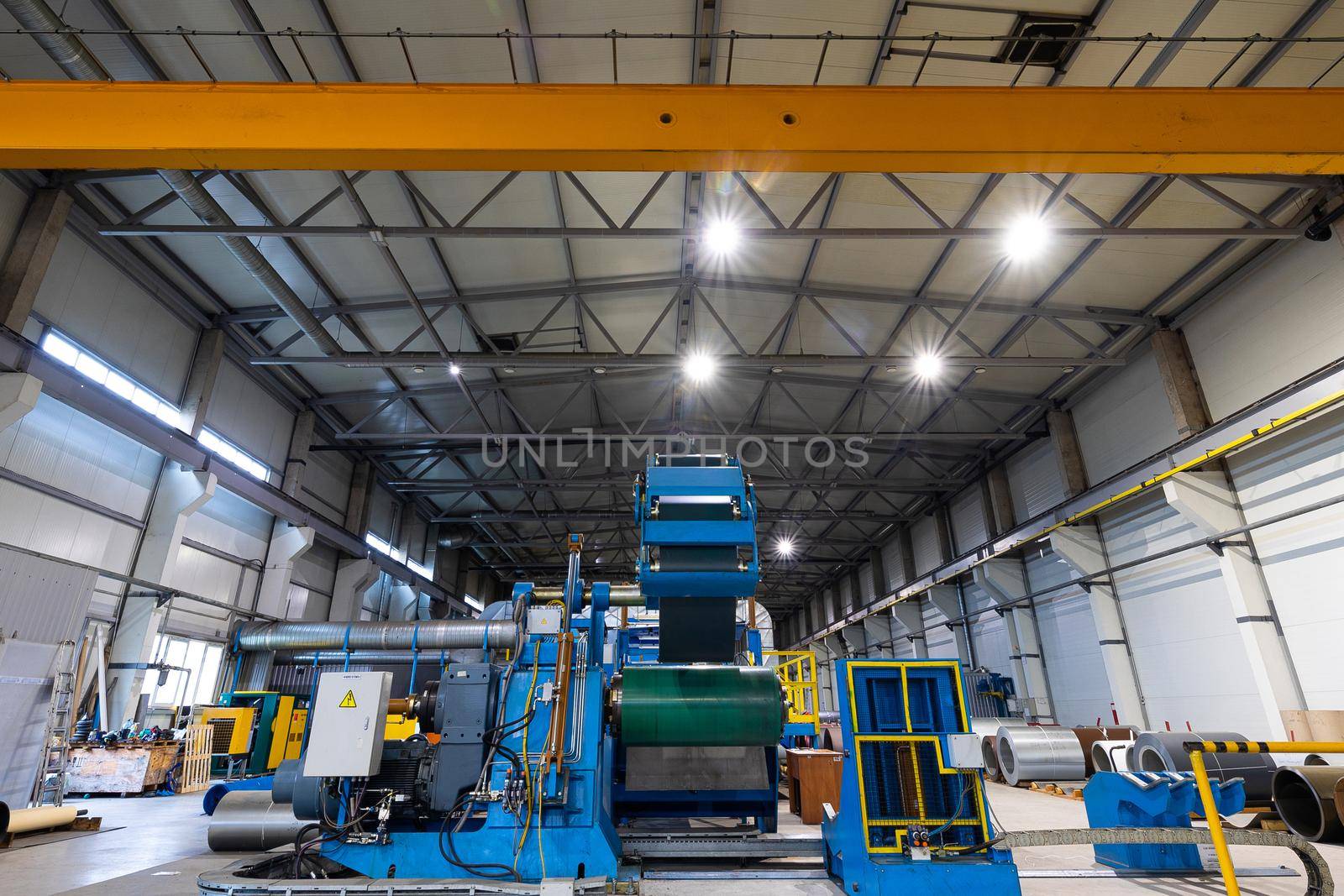 Metal sheet profile forming machine, process of making steel tile for roof, industrial manufacturing. Background of plant and factory.