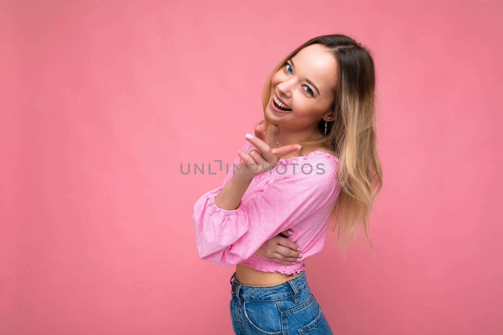 Young beautiful woman. Trendy woman in fashionable pink crop top. Positive female shows facial emotions. Funny model isolated on pink background with free space.
