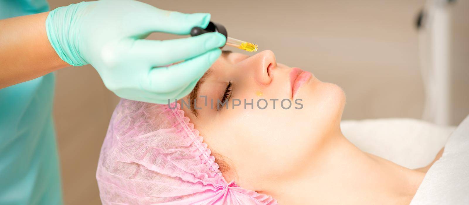 Young white woman getting acid organic retinol peel face skin with the pipette in a beauty clinic. by okskukuruza
