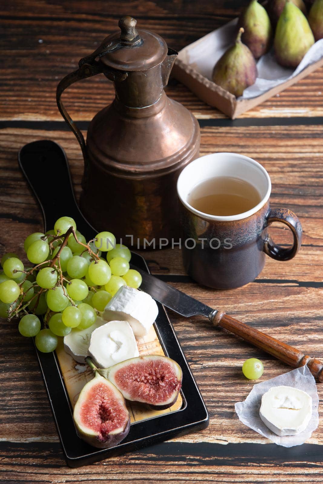 cheese plate with goat cheese, grapes and figs, copper teapot, angle view, healthy food, high-calorie breakfast. High quality photo