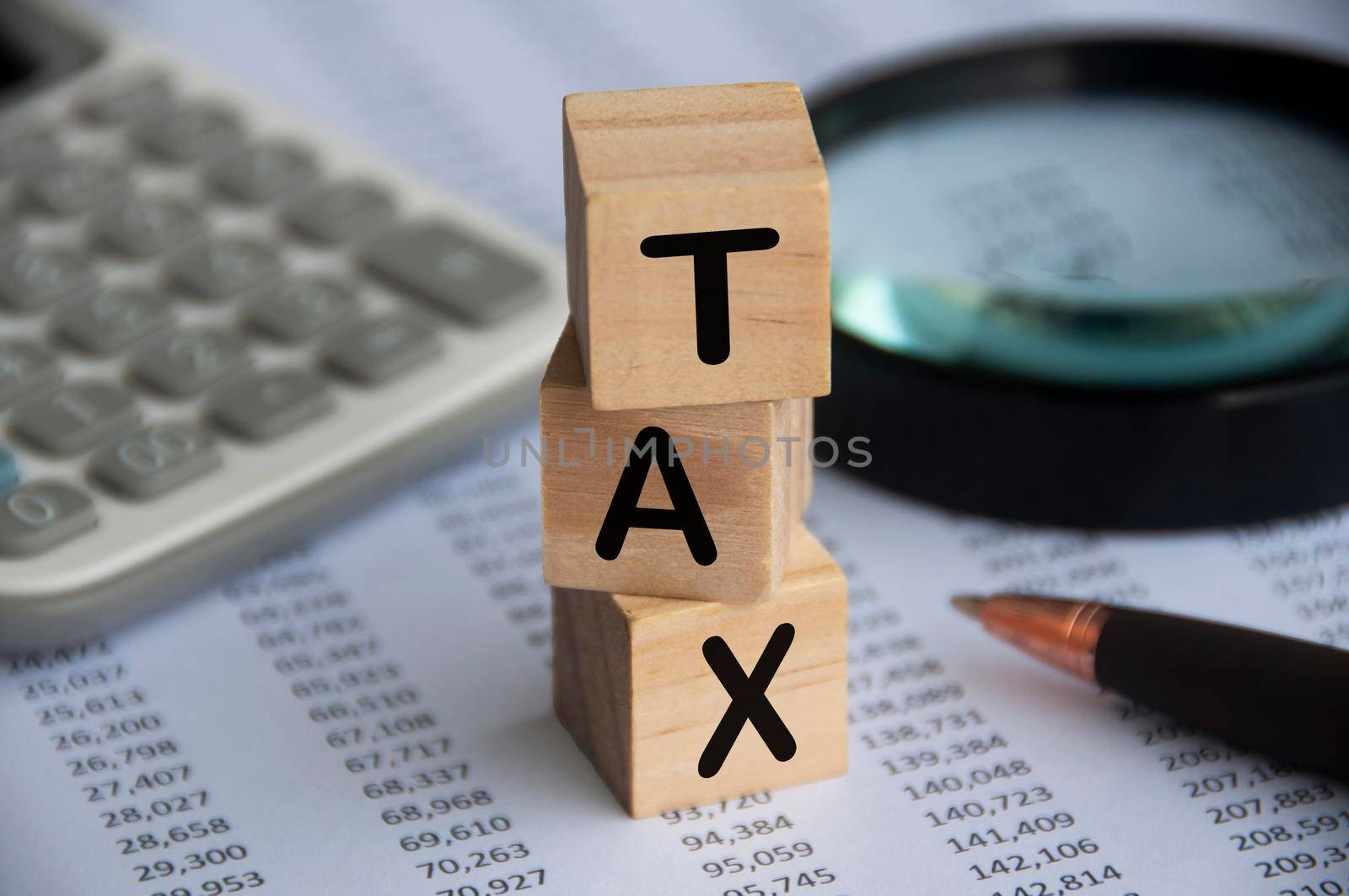 Tax word on wooden blocks with calculator, pen, magnifying glass and data analysis background. Tax concept.