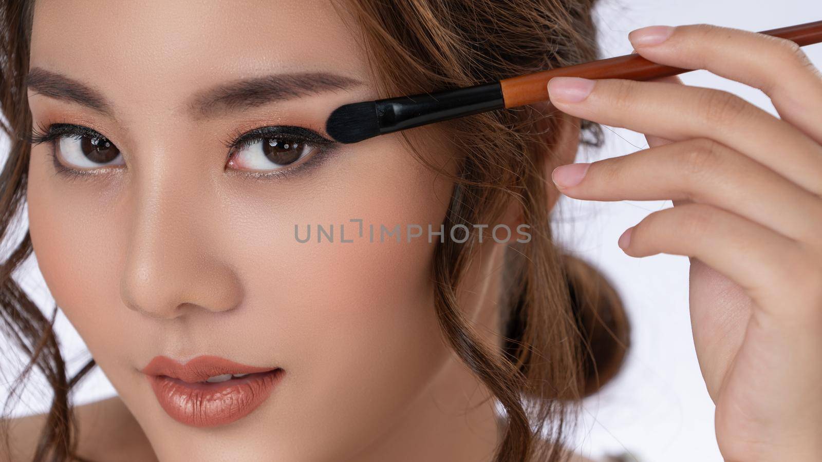 Closeup gorgeous young woman putting black mascara on her long eyelashes with brush. Beauty cosmetic concept. Female model with perfect skin.