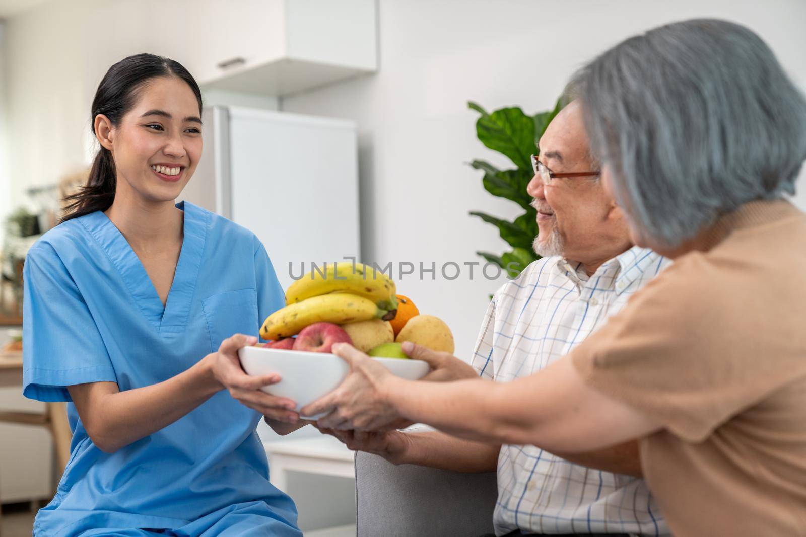 Contented senior couple taking a bowl of fruit from a nurse at home. by biancoblue