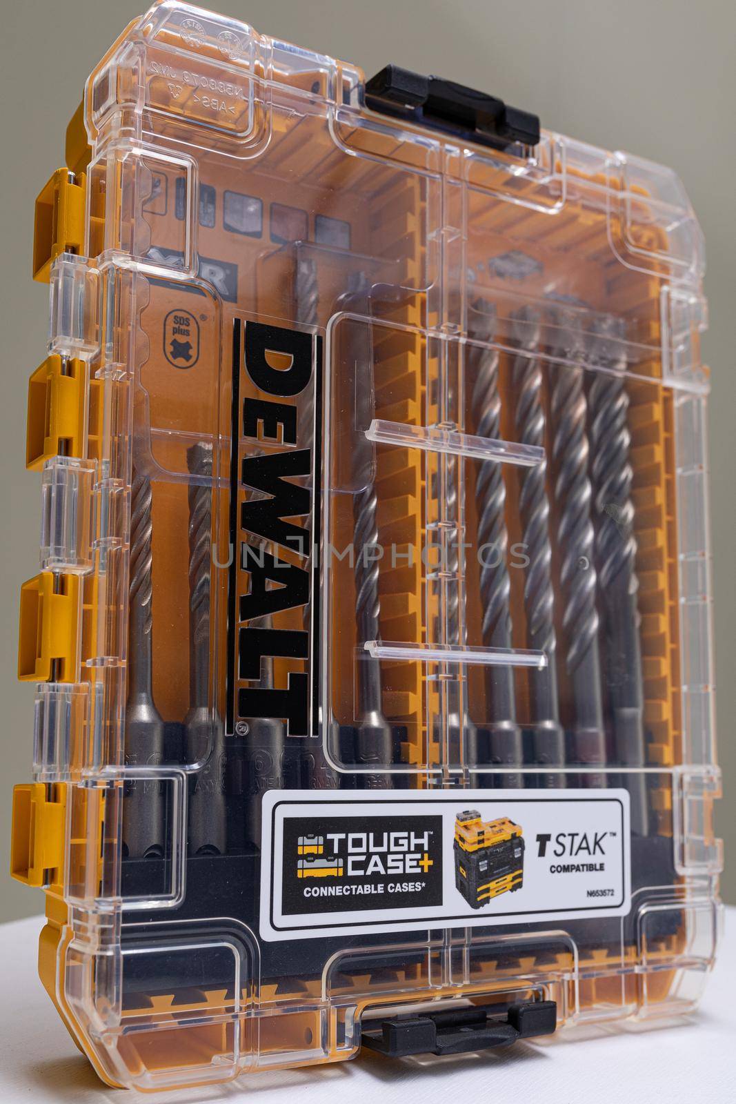 Vertical photo shot of yellow and transparent kit box with drills for drilling holes on a white table. Repair and construction concept by TRMK