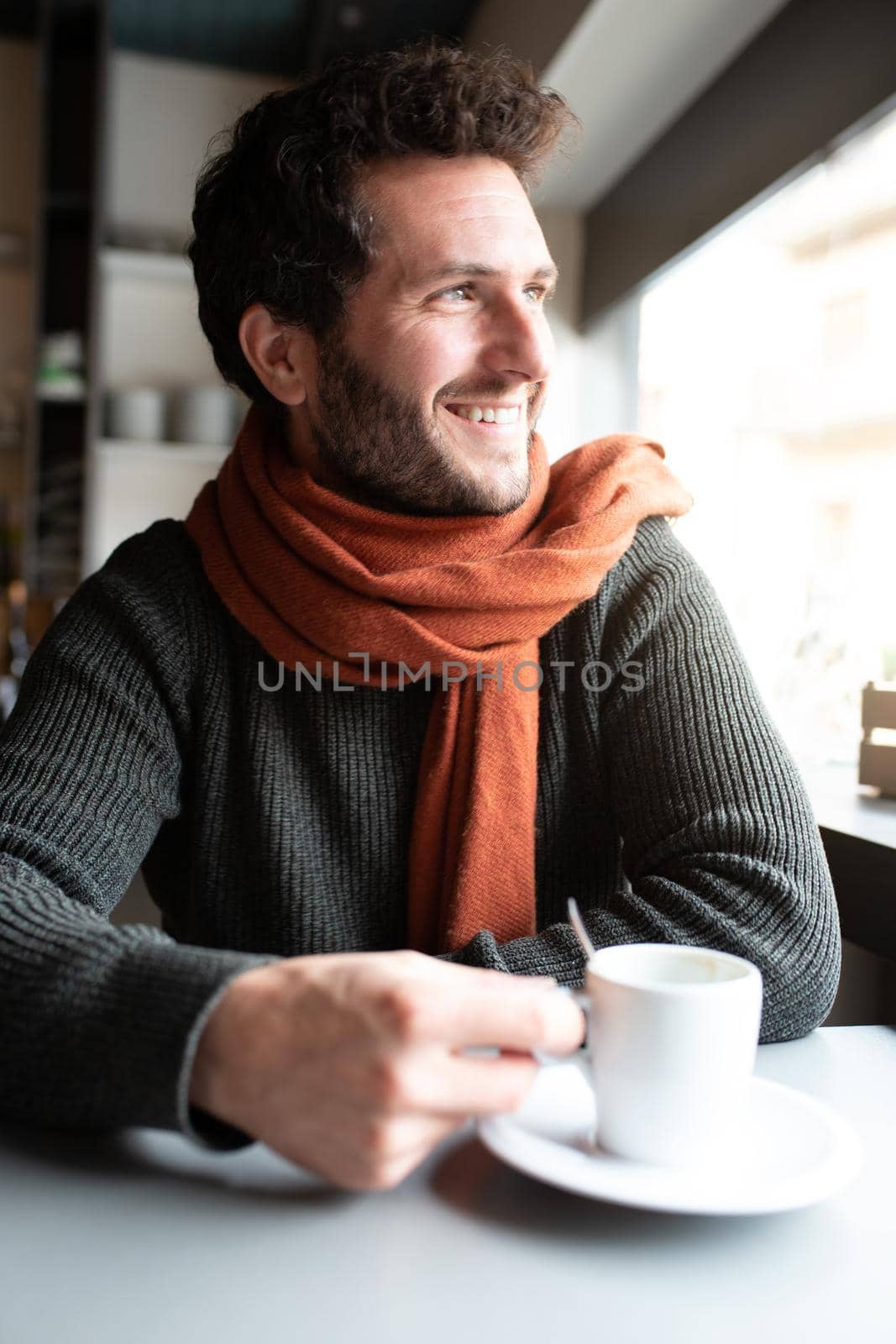 Vertical portrait of happy man having morning coffee in coffee shop looking out the window. Lifestyle concept.