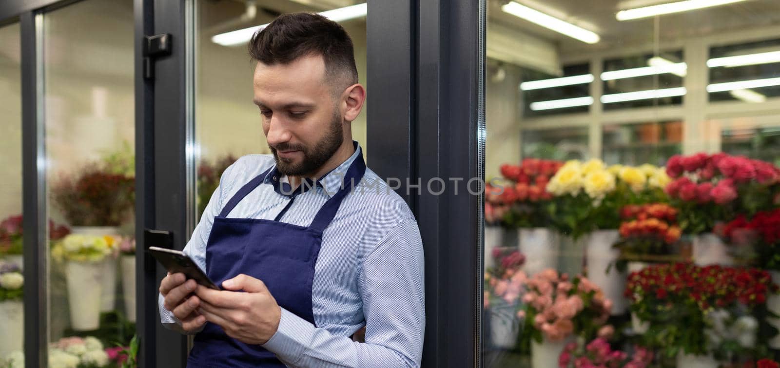 businesswoman florist looking at phone next to refrigerator with fresh flowers and bouquets.