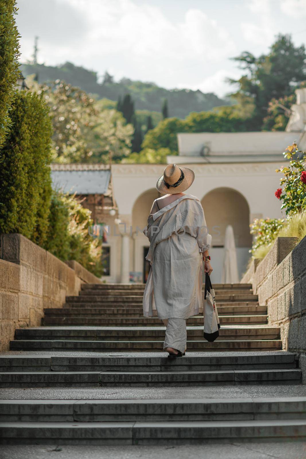 Woman on the stairs in the park. A middle-aged lady in a hat in a white outfit with a bag walks around the Livadia Palace.