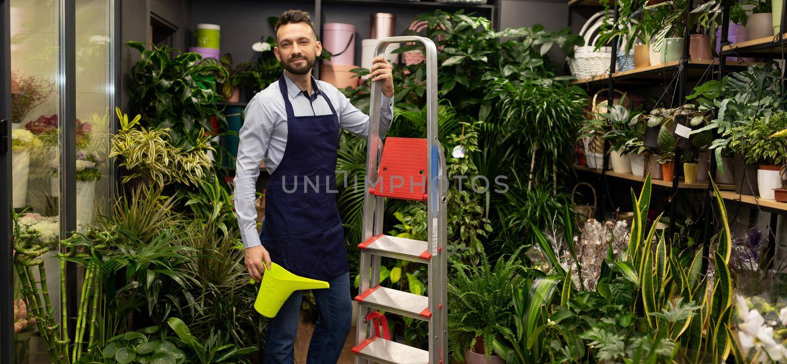 florist with a watering can in his hands and a stepladder on the background of a flower shop.