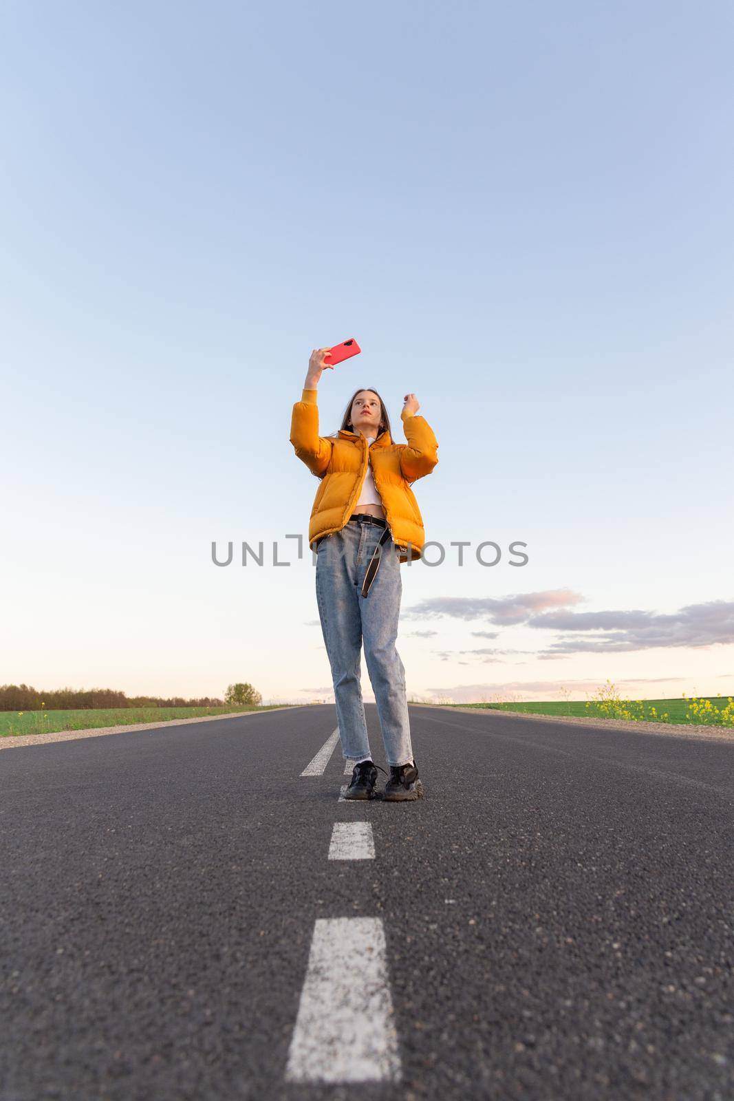 Cool modern teen girl poses on a lonely road while the sky background looks blue with clouds at sunset.