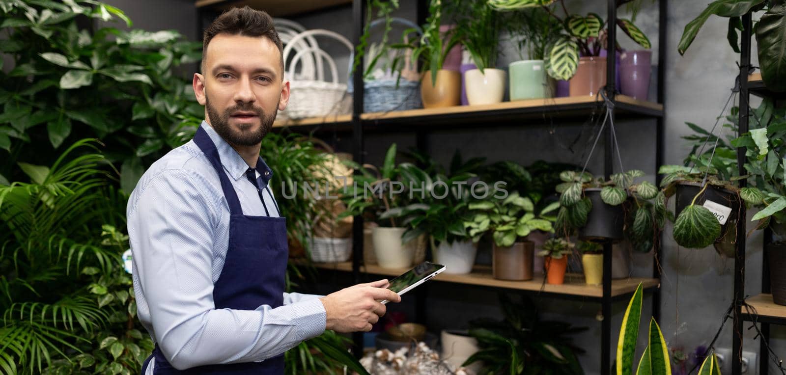 young entrepreneur florist with a tablet in his hands on the background of a flower shop.