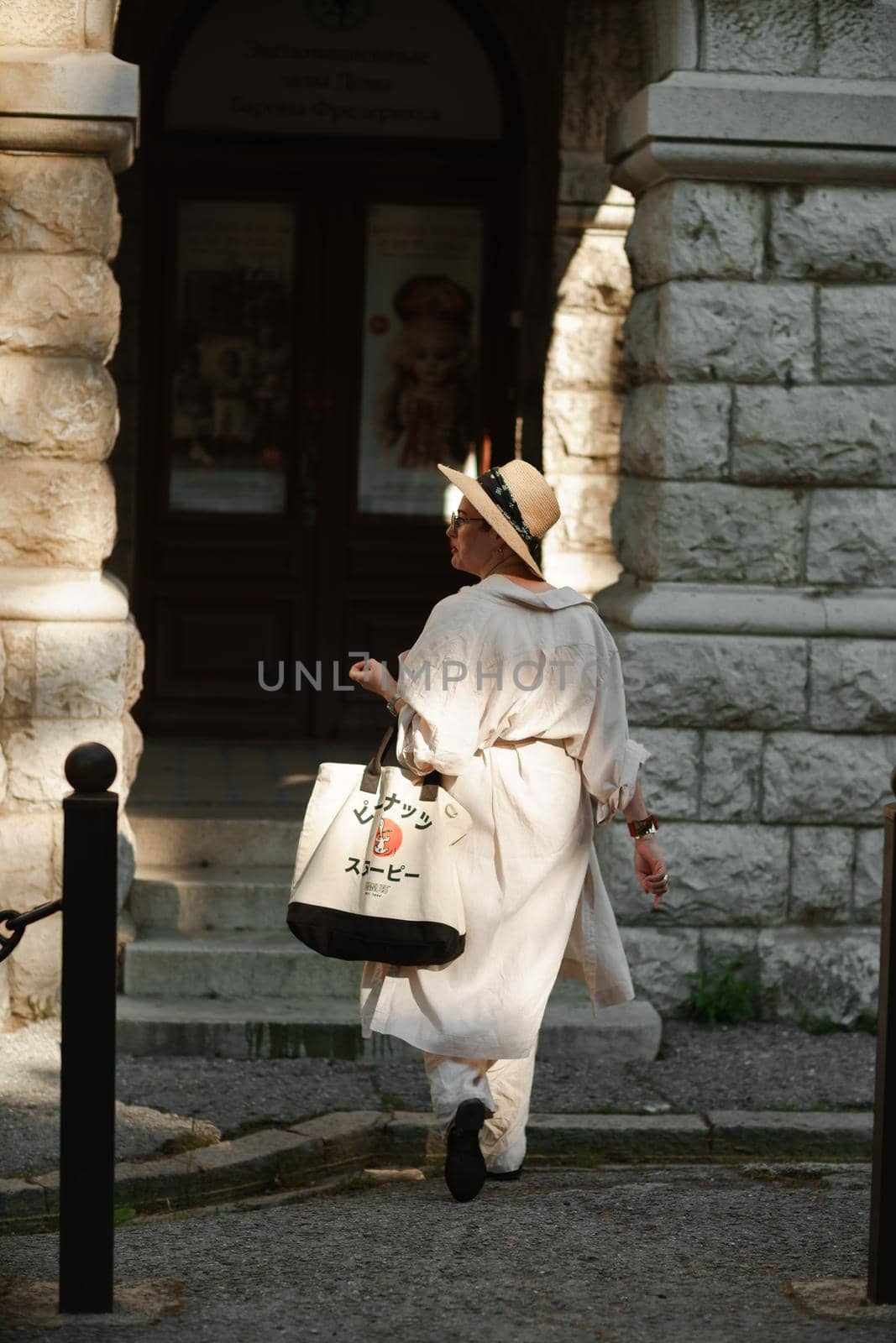 A woman in a hat in a white outfit with a bag walks around the Livadia Palace.