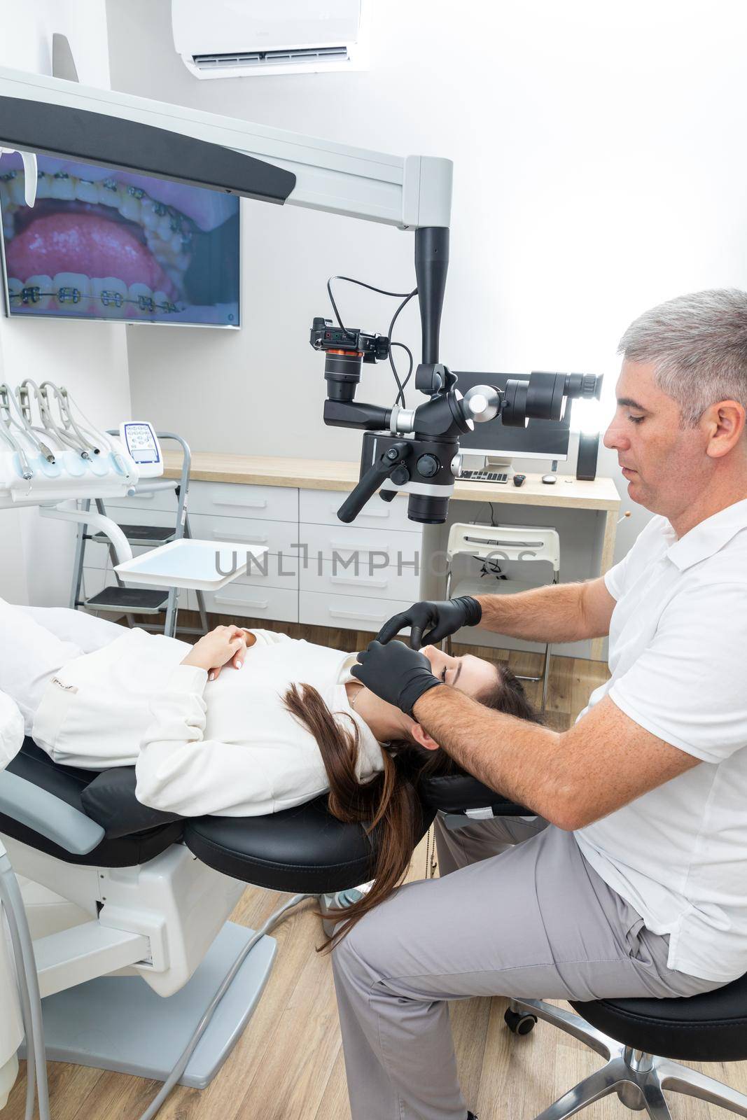 Dentist using dental microscope treating patient dental clinic office. Medicine, dentistry and health care concept by Mariakray