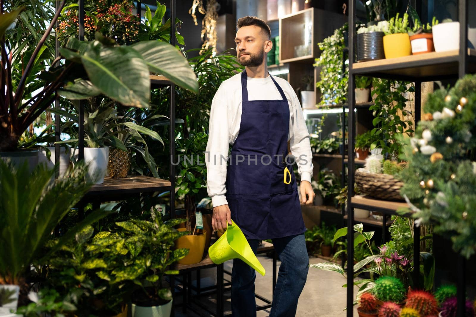 male florist In the garden center with a watering can For wildflowers in his hands.