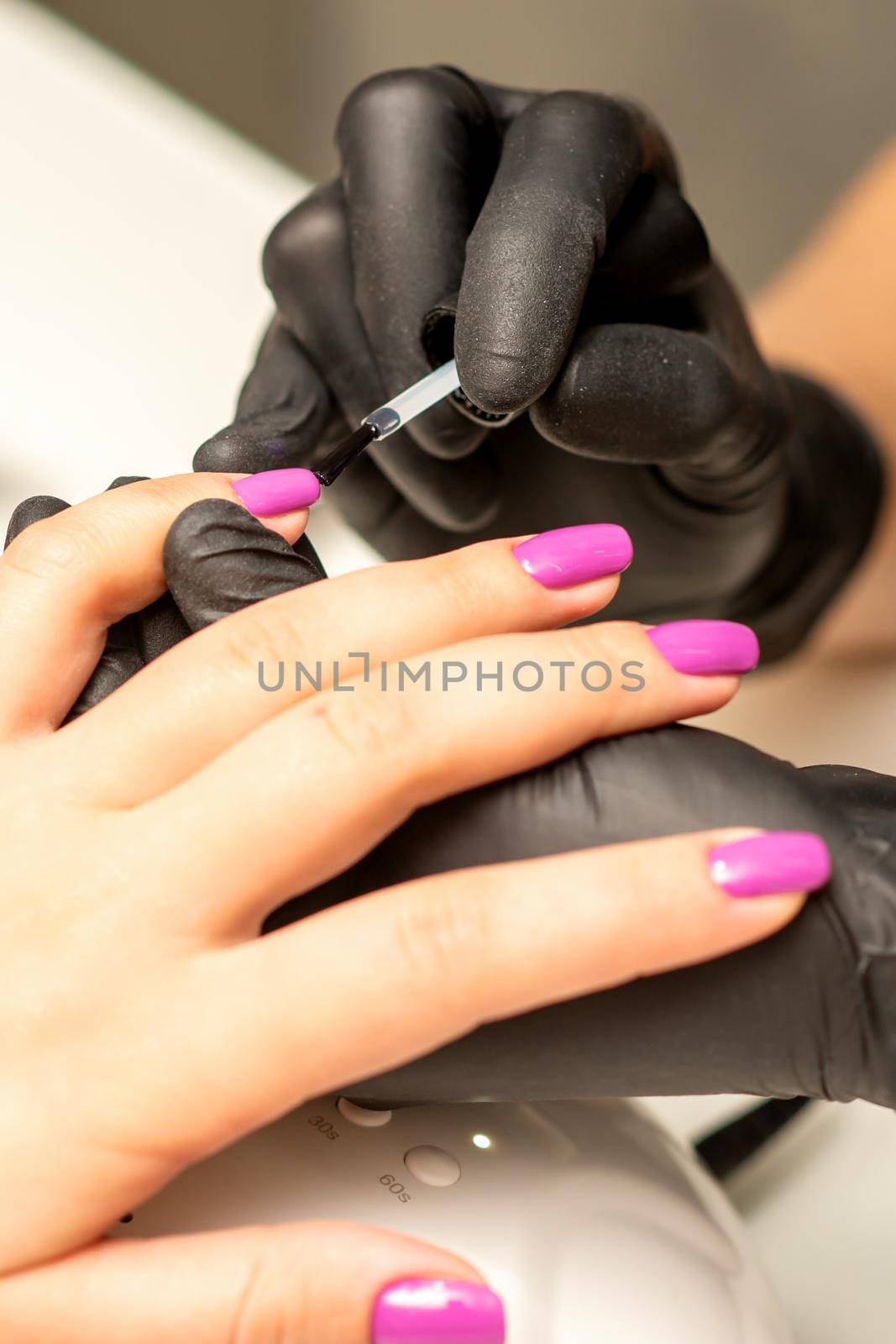 Professional manicure. A manicurist is painting the female nails of a client with purple nail polish in a beauty salon, close up. Beauty industry concept. by okskukuruza