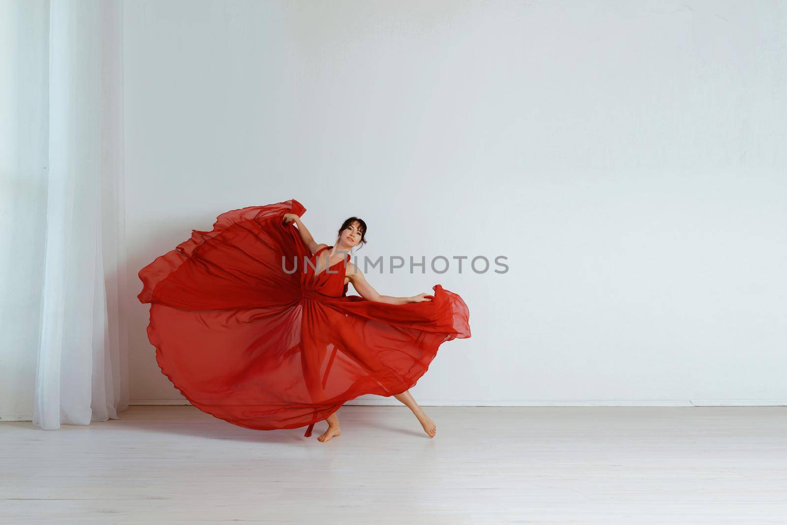 Dancer in a red flying dress. Woman ballerina dancing on a white studio background.