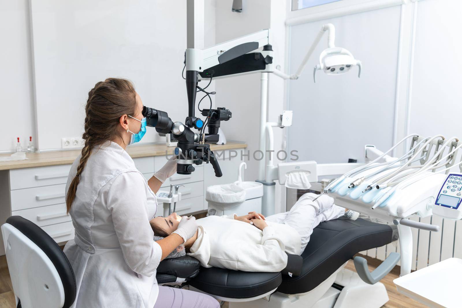 Female dentist using dental microscope treating patient teeth at dental clinic office. Medicine, dentistry and health care concept