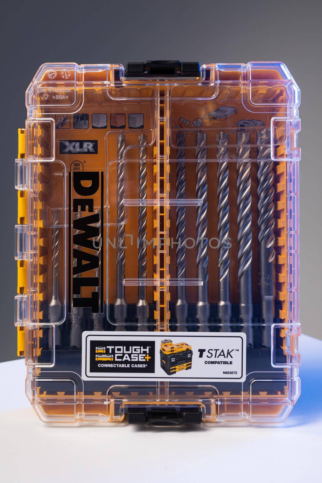 Vertical photo shot of yellow and transparent kit box with drills for drilling holes on a white table and isolated on background. Repair and construction concept.