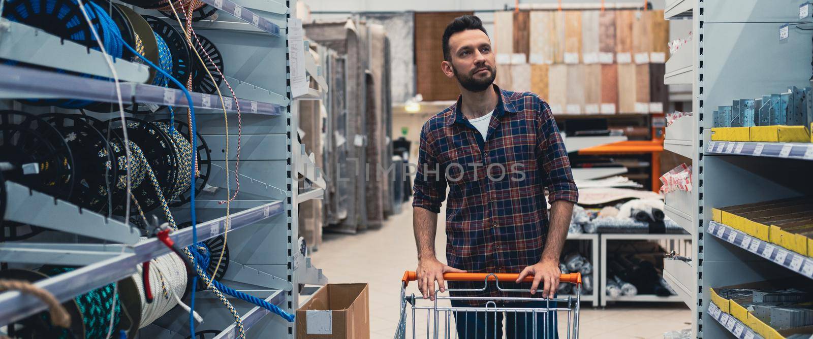 a buyer in a hardware store walks between the aisles with goods with a trolley.