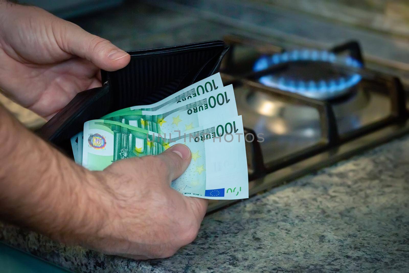 Close up of mens hands with a purse and euro banknotes on the background of a gas stove. A concept showing the energy crisis in Europe. Copy space