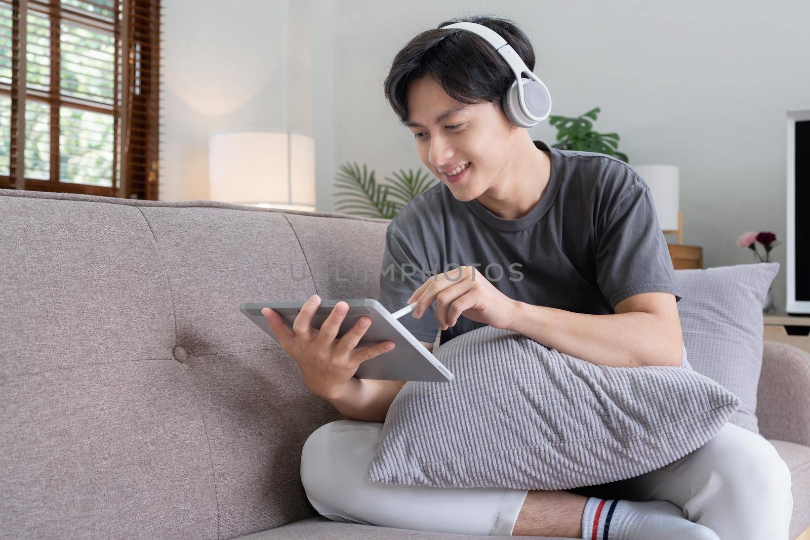 Attractive smiling young man using tablet and listen music on sofa at home. lifestyle concept.