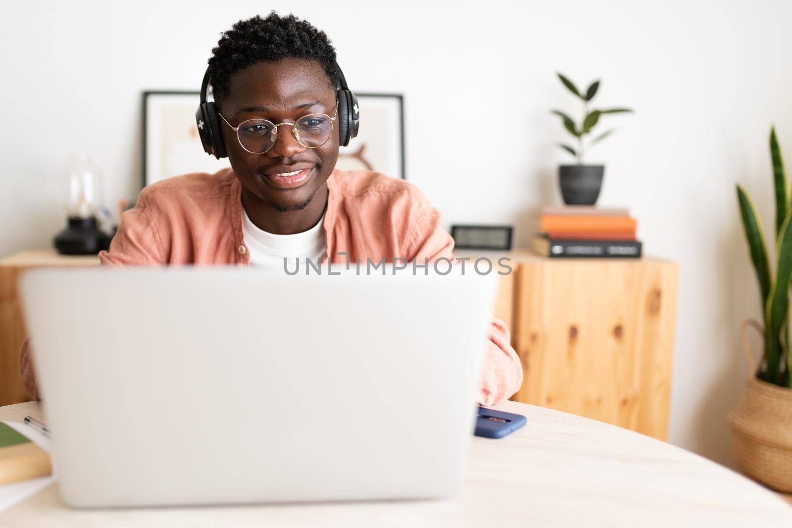 Front view of young African American man wearing headphones working, studying at home using laptop. Copy space. E-learning and technology concept.