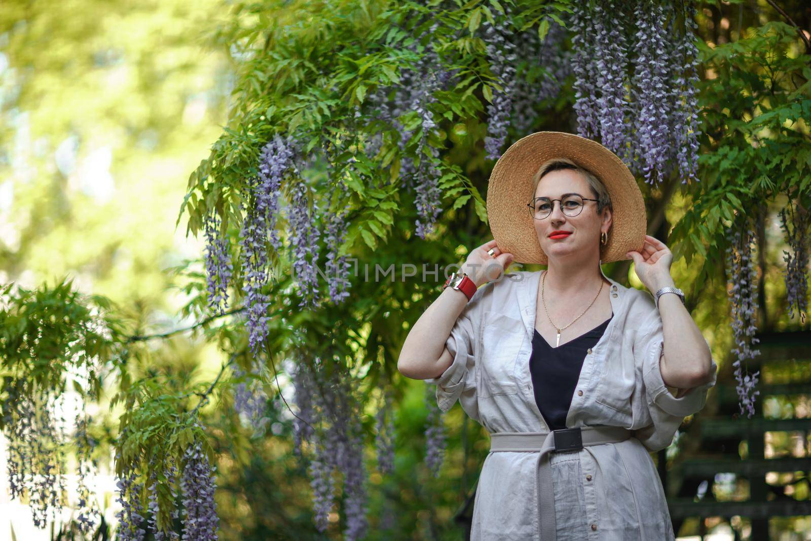 Thoughtful happy mature woman in hat surrounded by chinese wisteria by Matiunina