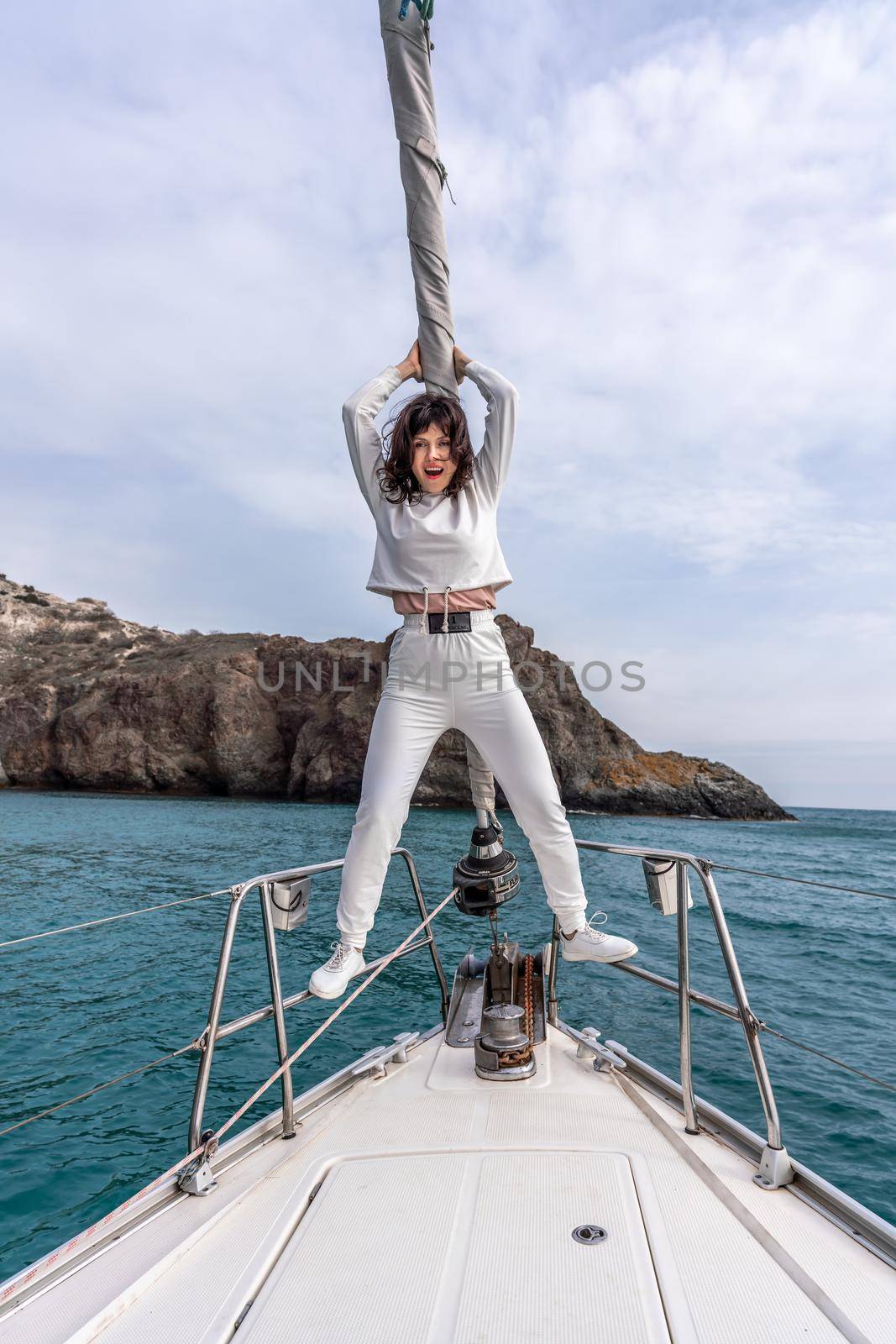 Woman standing on the nose of the yacht at a sunny summer day, breeze developing hair, beautiful sea on background.