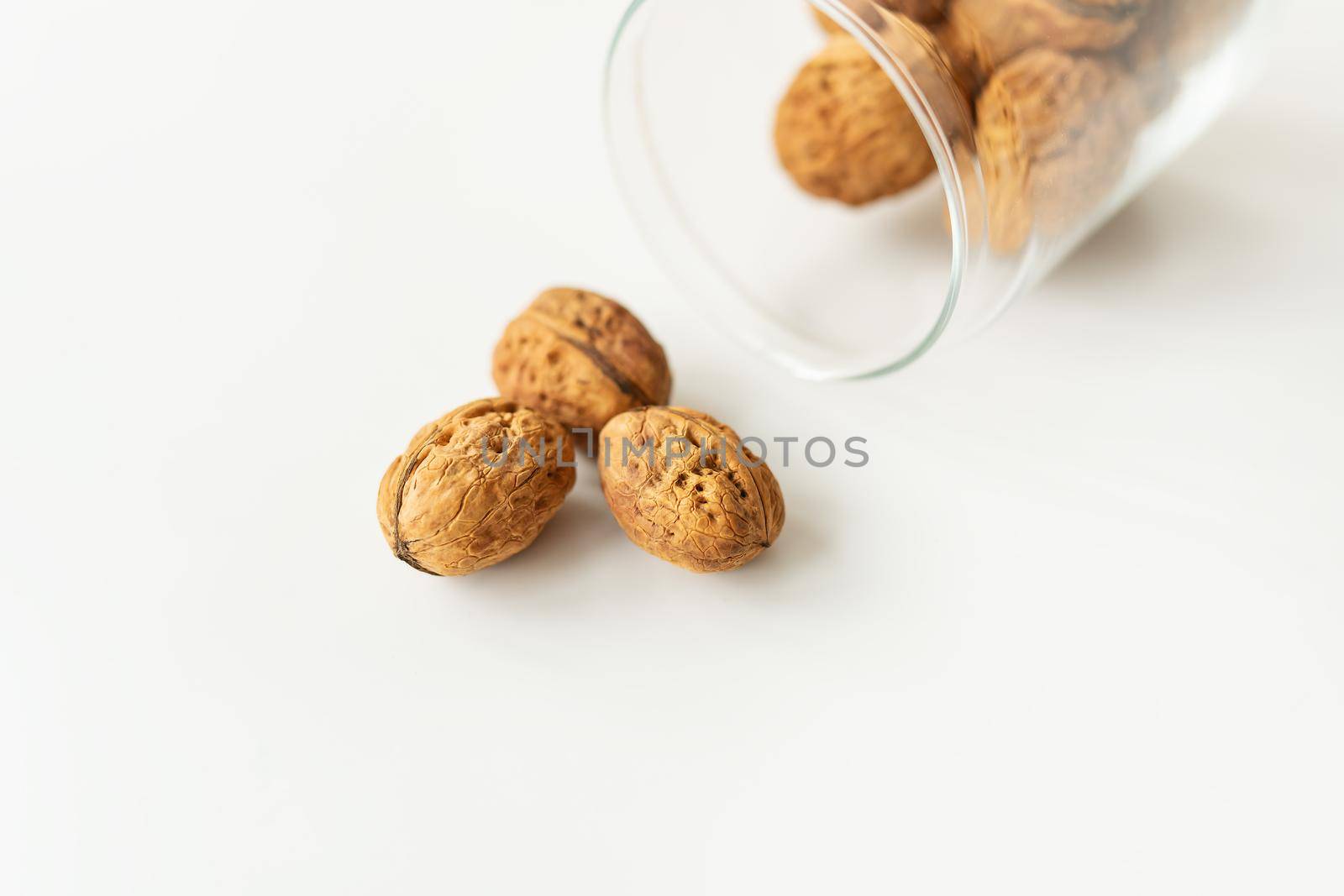 Beautiful whole walnut kernels in a glass jar, whole nuts in shell spilling on the table. Selective focus, noise