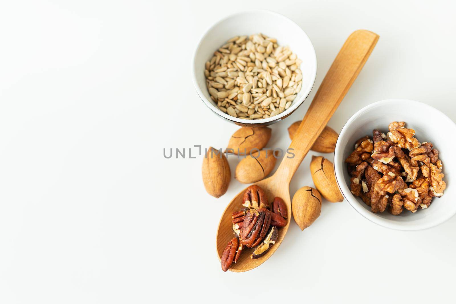 A close-up of a plate with different nuts and seeds along with a wooden spoon lie on a white table. The concept of weight loss, healthy eating, overweight. Fitness menu