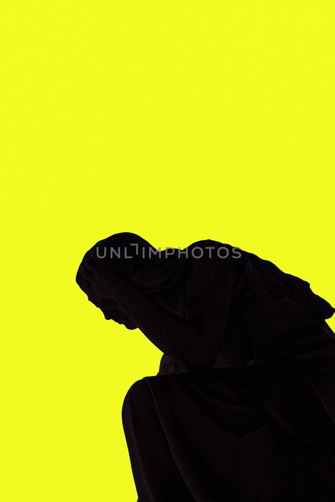 Statue shadow silhouette of an angel holding head with hand, against a strong yellow background.