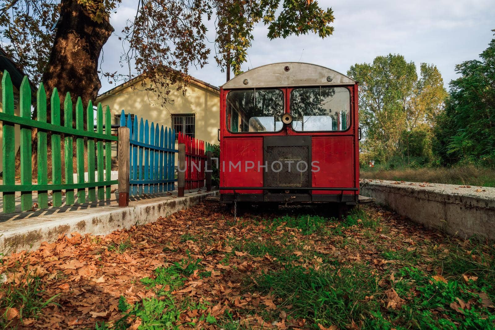 Deserted train station with multi-color painted wooden railings and old small red wagon left on empty rail track covered with fallen leaves.