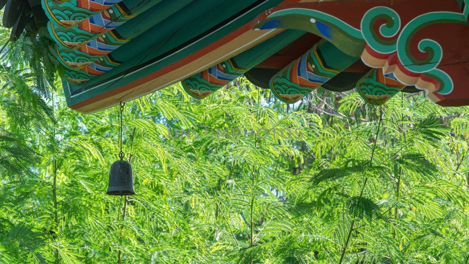 A bell on the roof of a Buddhist scar against a backdrop of green trees by voktybre