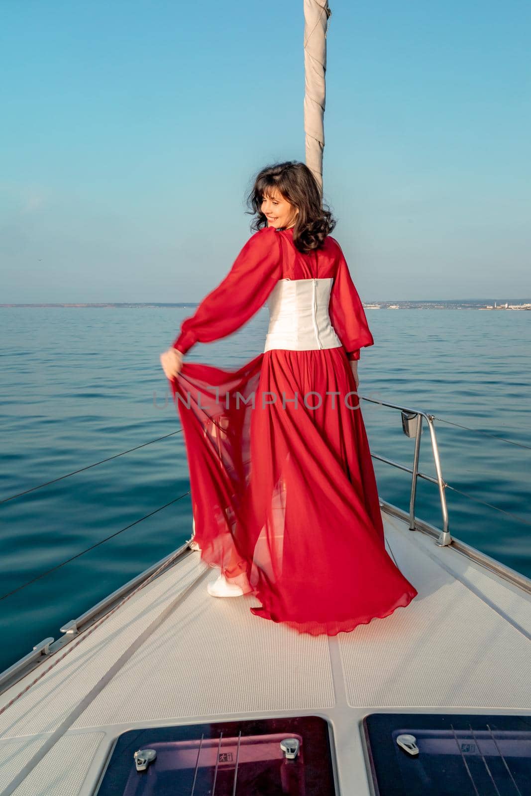 Attractive middle-aged woman in a red dress on a yacht on a summer day. Luxury summer adventure, outdoor activities. by Matiunina