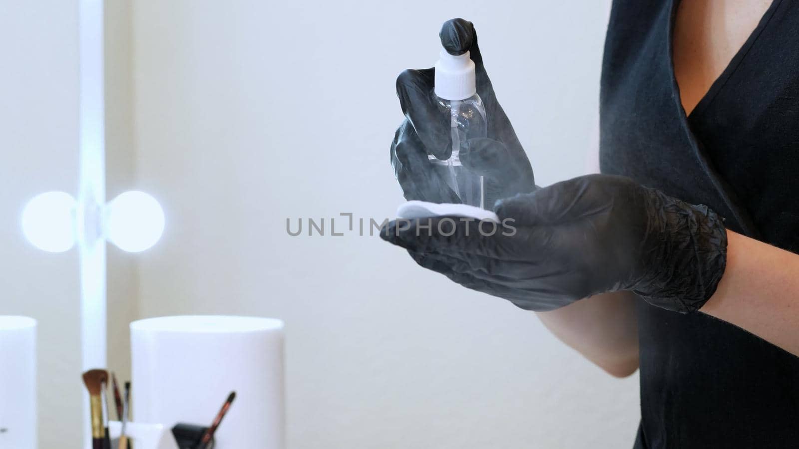 beauty saloon. close-up, the master in black special gloves holds a cotton pad and sprinkles it with an antiseptic. High quality photo