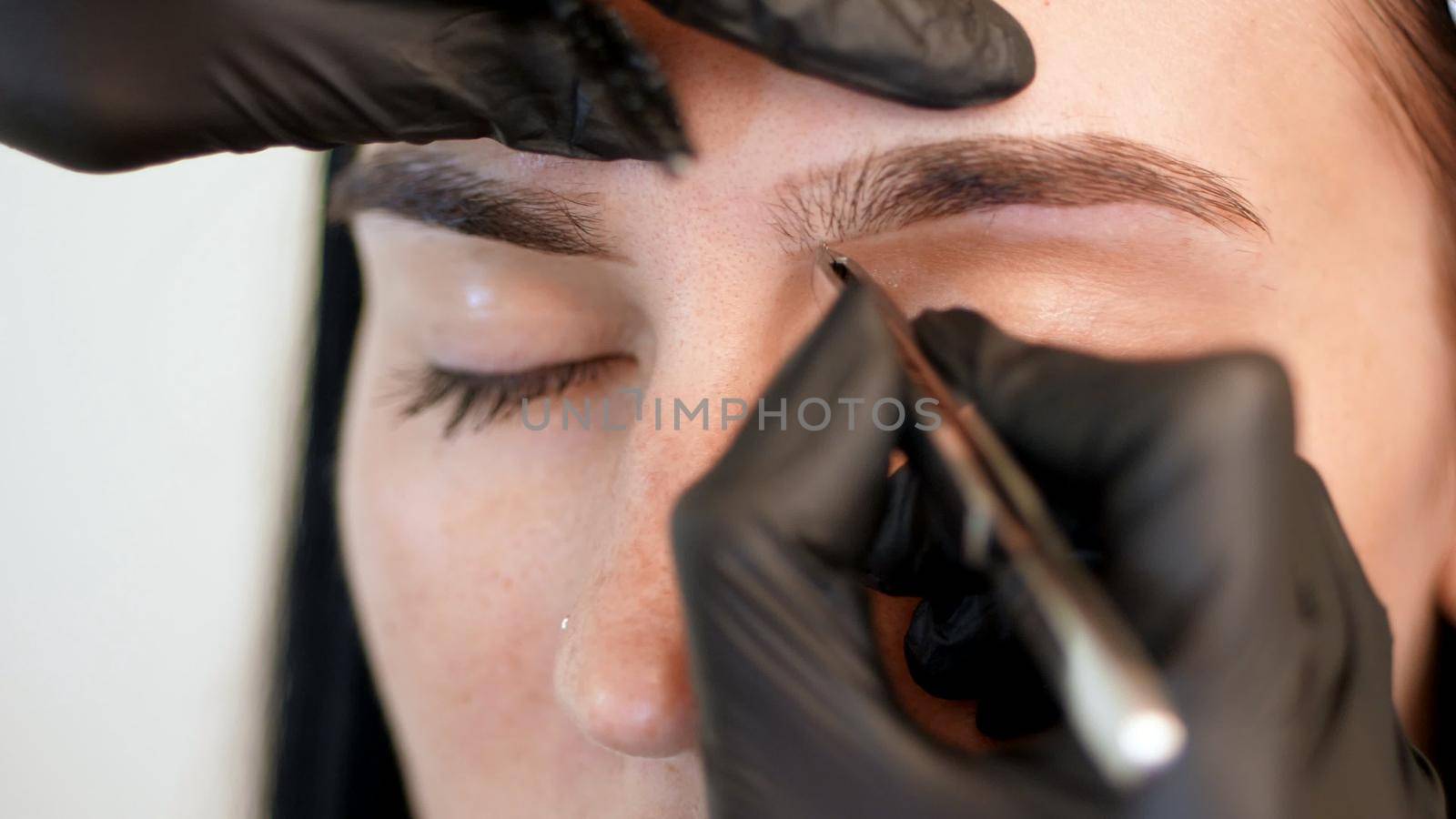 beauty saloon. close-up, hands of the cosmetician in black rubber gloves hold tweezers and pull out eyebrows. Master corrects the shape of the eyebrows. High quality photo