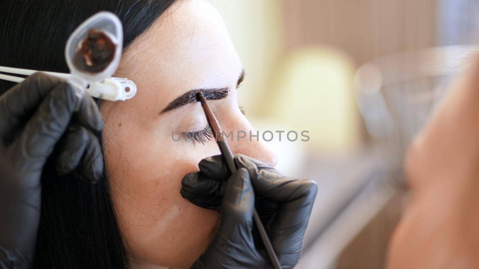 close up. young woman gets eyebrow correction procedure. kosmetolog- makeup artist applies paint with brush on eyebrows in beauty saloon. Professional care for face. High quality photo