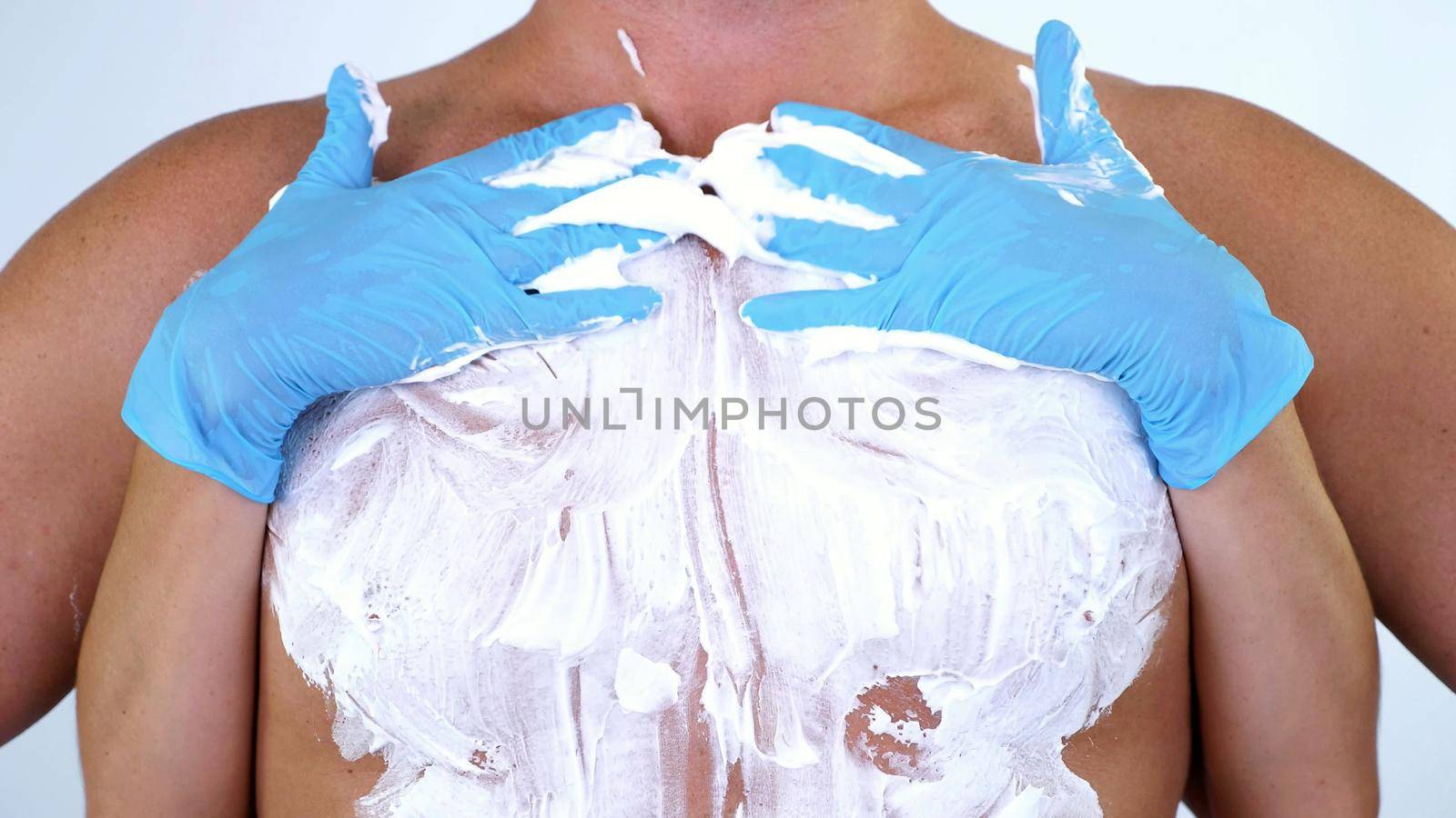 Close-up, cosmetologist female hands in gloves spread white shaving foam on Naked hairy male Torso, chest sexually. on white background. High quality photo