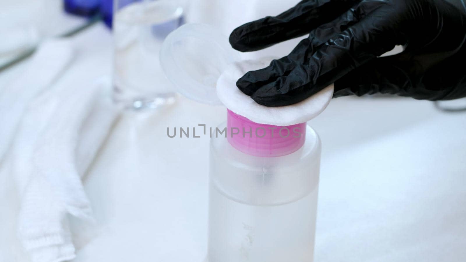 close-up, the hands of the beautician in black rubber gloves hold the cotton pad and moisten it in a special transparent liquid from the bottle with a dispenser. High quality photo