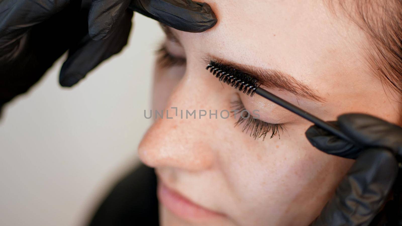beauty saloon. close-up, hands of the cosmetician in black rubber gloves keep a special brush and comb eyebrows. Master corrects the shape of the eyebrows. Professional care for face. High quality photo