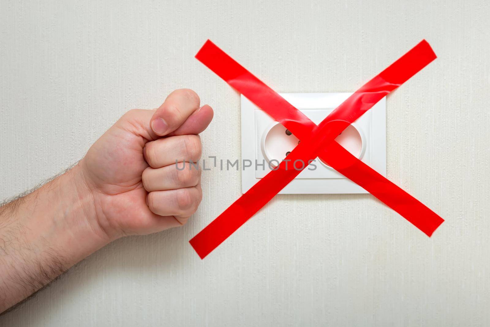 The man shows a fig gesture near the electrical outlet, tied with a red ribbon criss-cross. The concept of the energy crisis in Europe