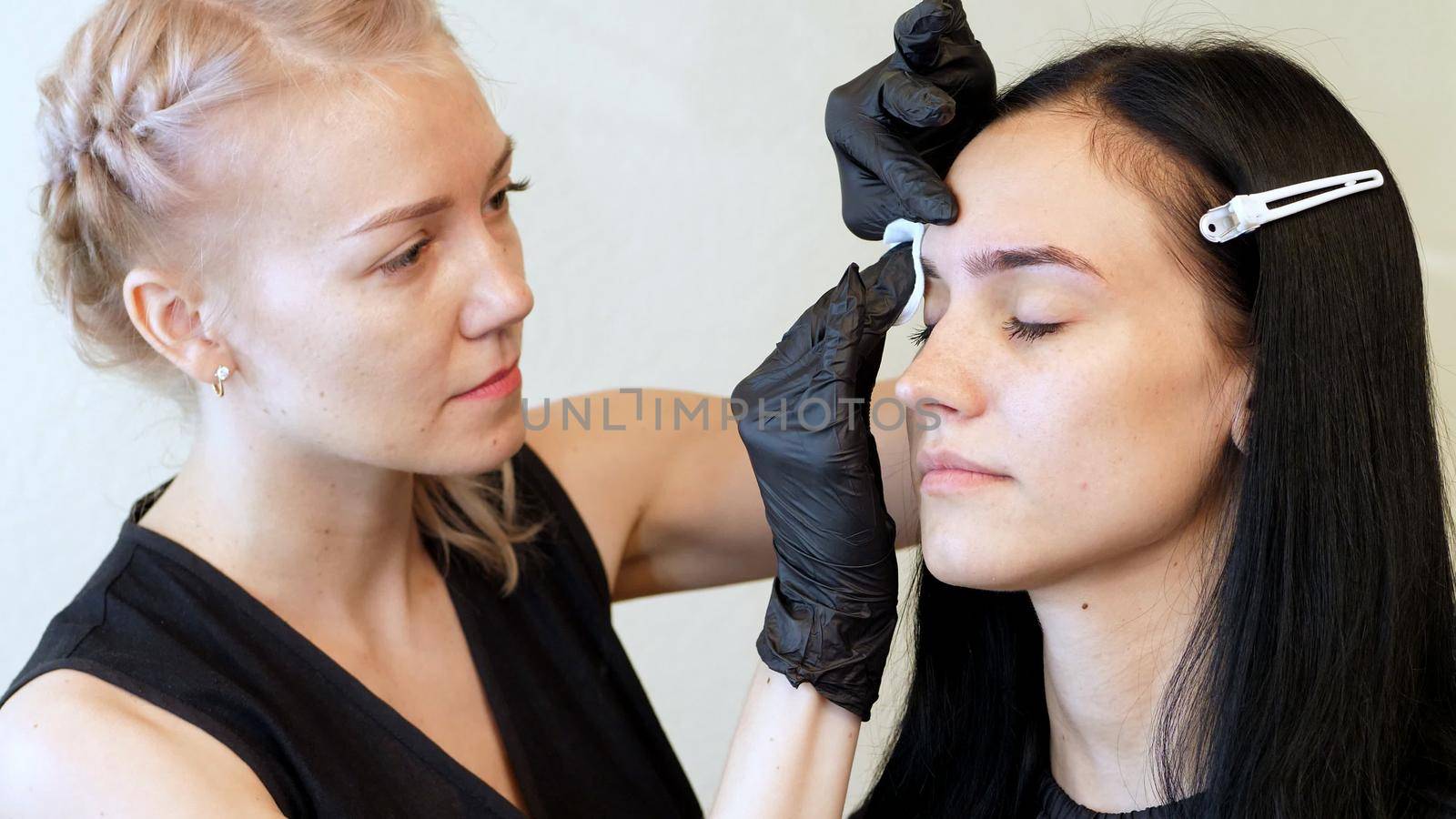 beauty saloon. the master wipes the eyebrow area with a cotton disc moistened with antiseptic. High quality photo