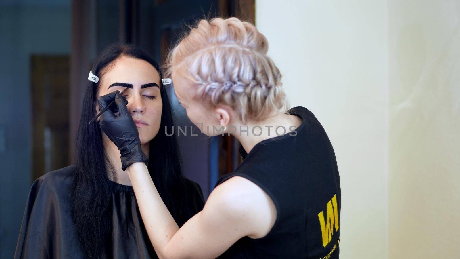young woman gets eyebrow correction procedure. kosmetolog- makeup artist applies paint with brush on eyebrows in beauty saloon. Professional care for face. High quality photo