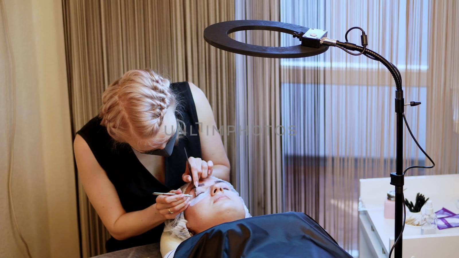 beauty saloon. procedure for eyelash extension. The master in the bandage on the face, glues each cilium with special glue, works by means of two tweezers. High quality photo